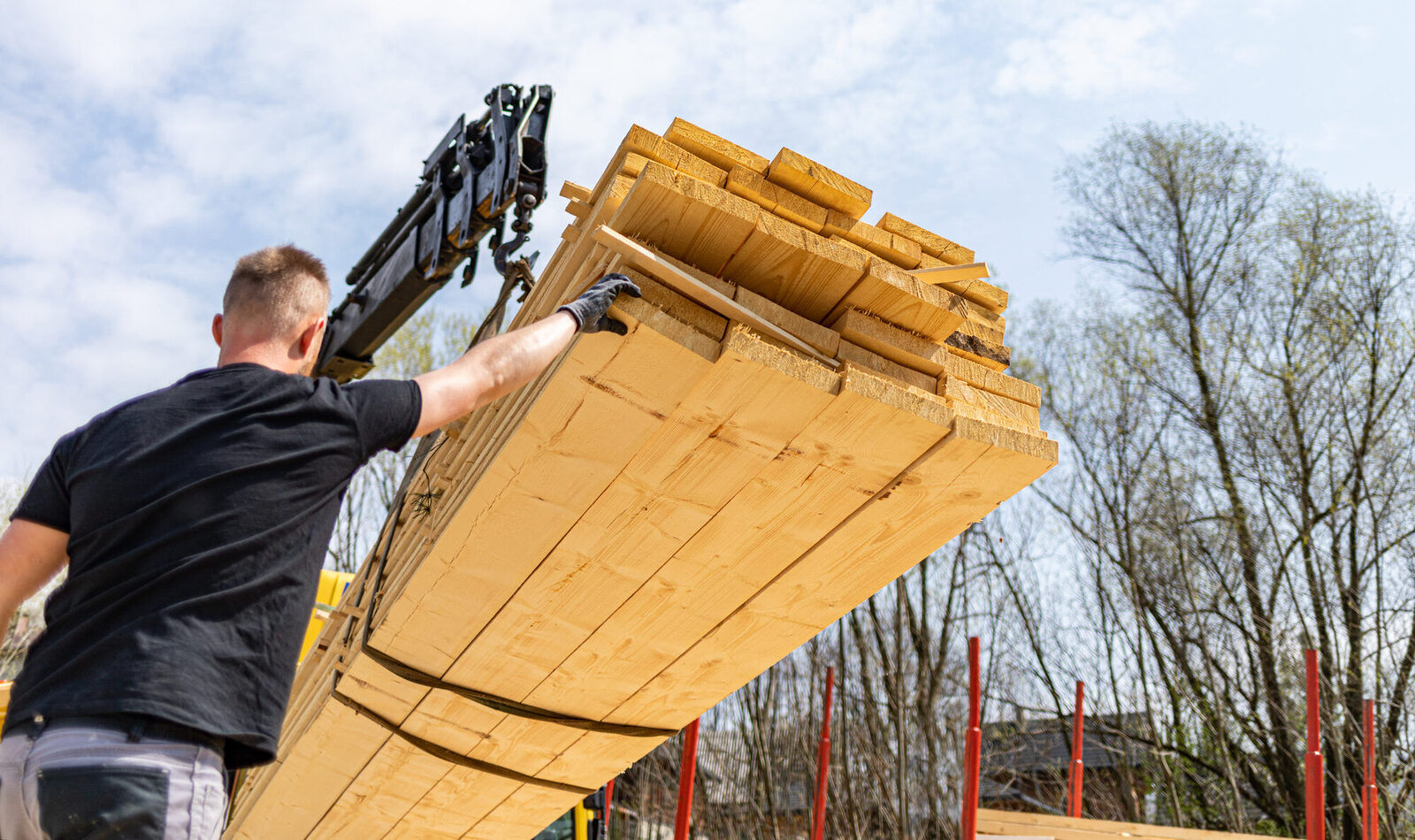 Dachdecker entlädt Holzbalken vom LKW mit Kran